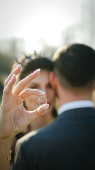 A bride elegantly showcases her engagement ring with the groom in the background, symbolizing love and commitment.