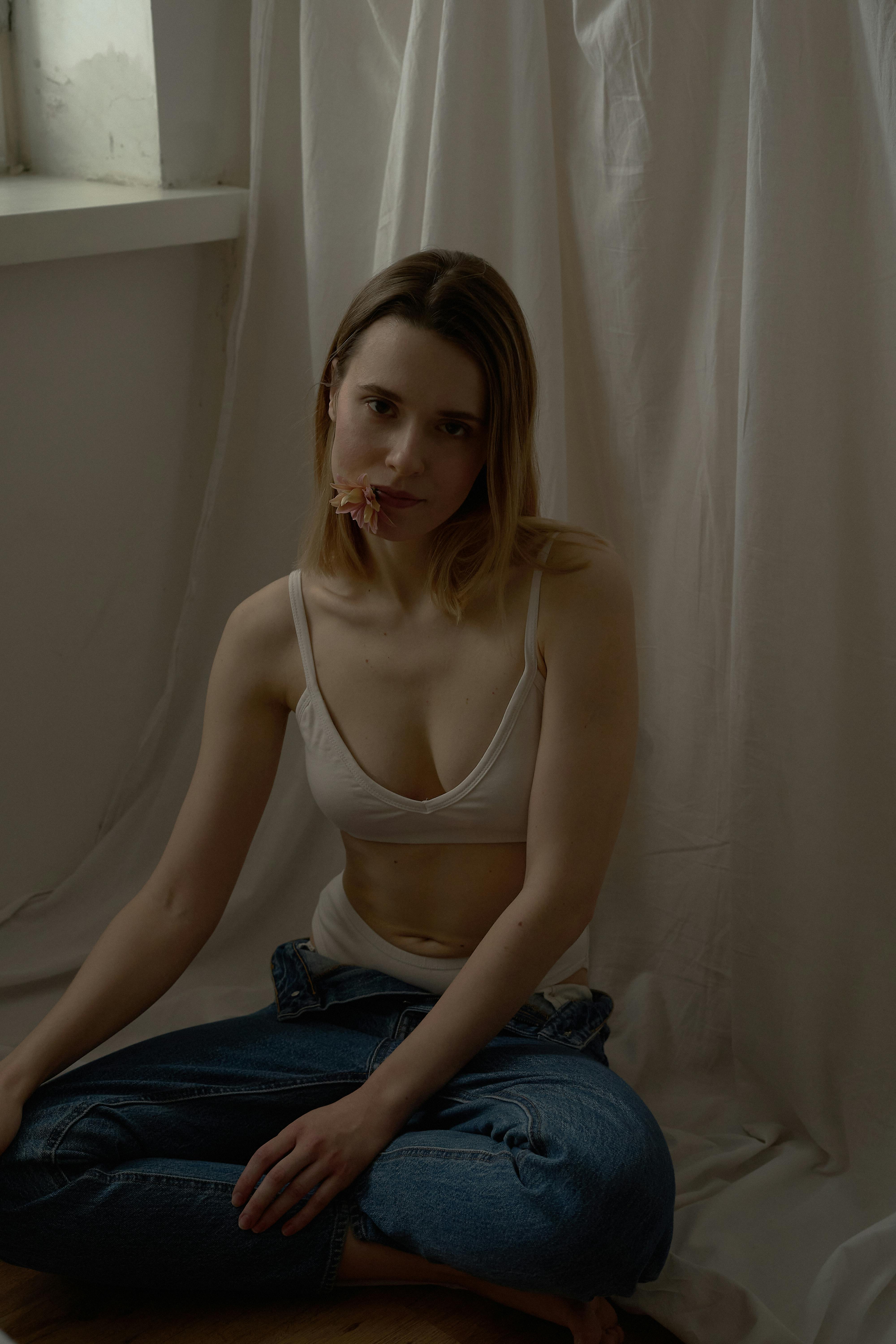 A contemplative woman in casual attire sits indoors against a draped background.