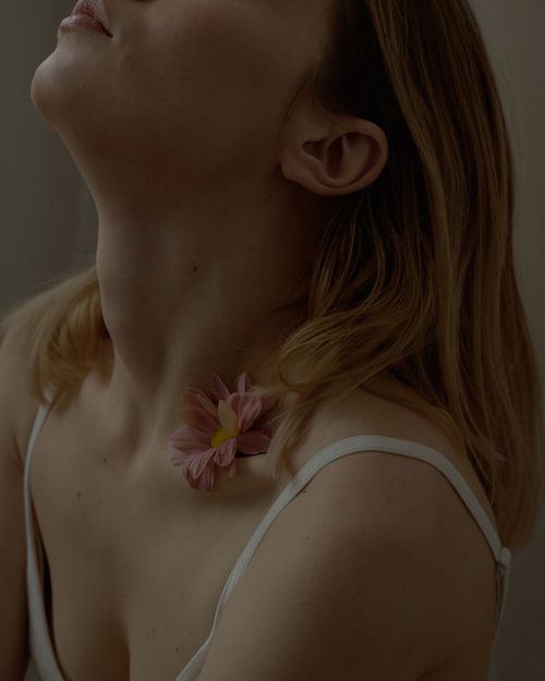 Free Close-up portrait of a young woman with a flower resting on her collarbone, exuding elegance. Stock Photo