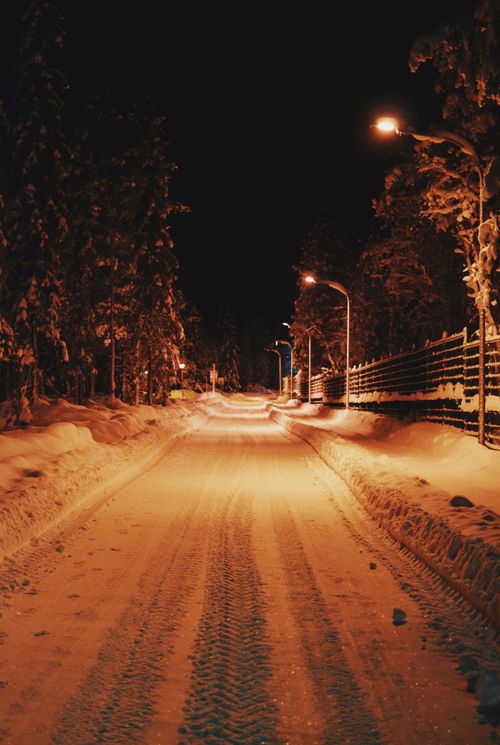 Free A winter scene of a snow-covered road illuminated by street lights, creating a warm ambiance. Stock Photo