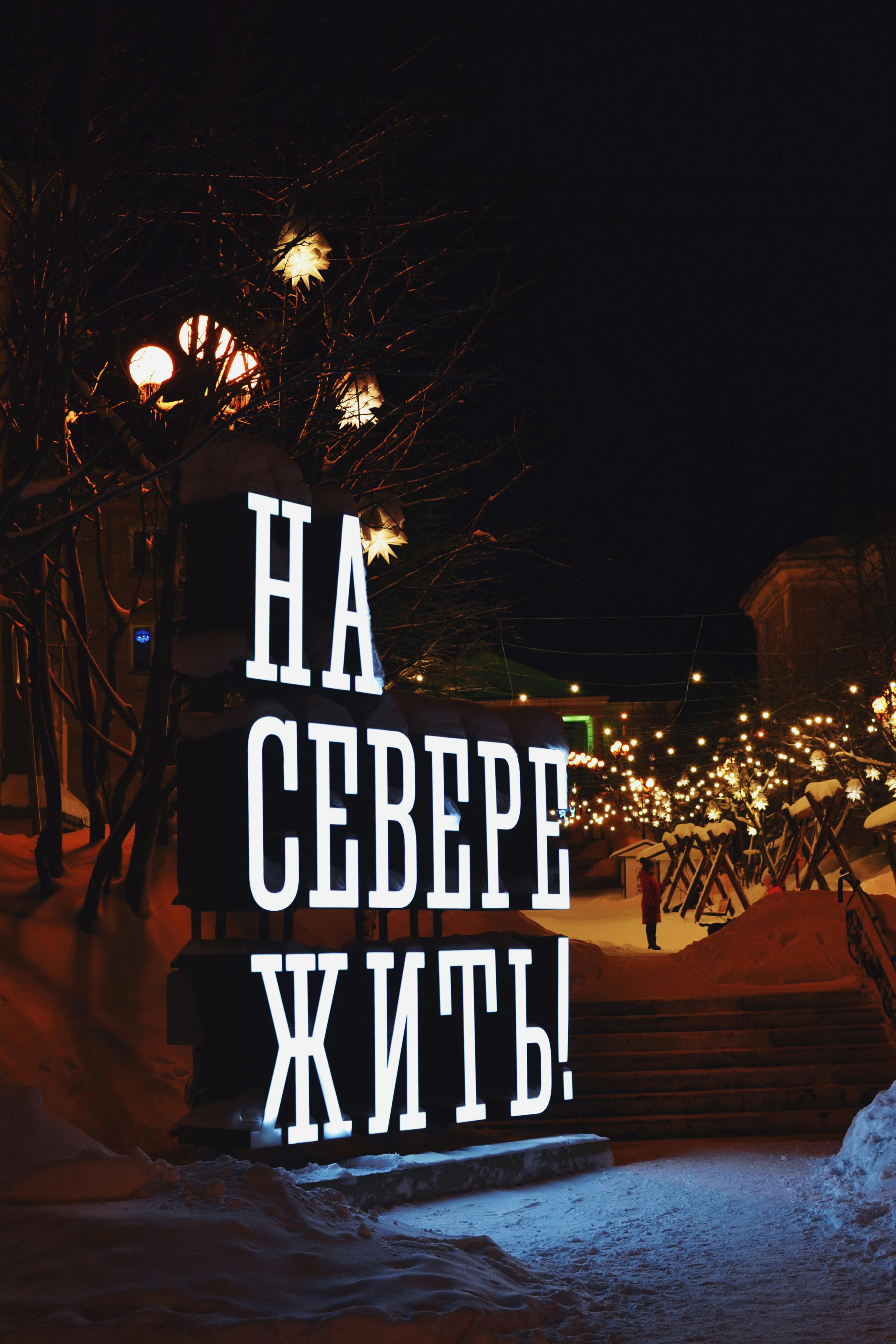 Brightly illuminated sign in a snowy urban setting at night, evoking a winter holiday atmosphere.