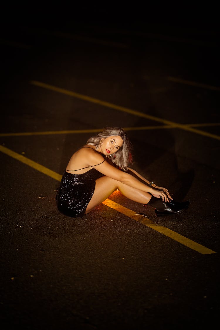 Woman In Glitter Dress Sitting On Ground On Parking Lot