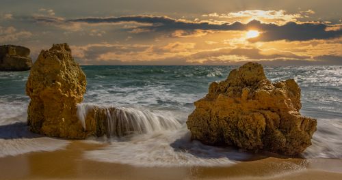 Free Captivating view of a sunset over the ocean with rocks and gentle waves. Stock Photo