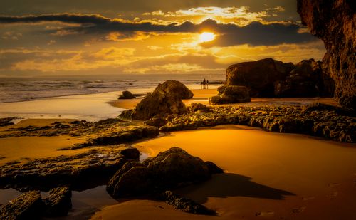 Free Dramatic sunset over a rocky beach, perfect for serene landscape lovers. Stock Photo