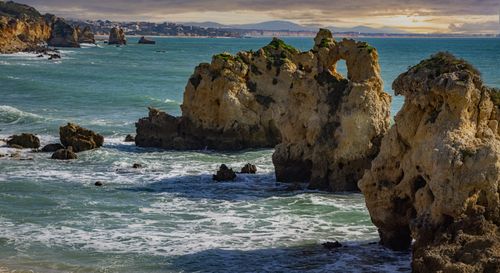 Free A picturesque seascape featuring rugged rock formations and gentle ocean waves on a cloudy day. Stock Photo