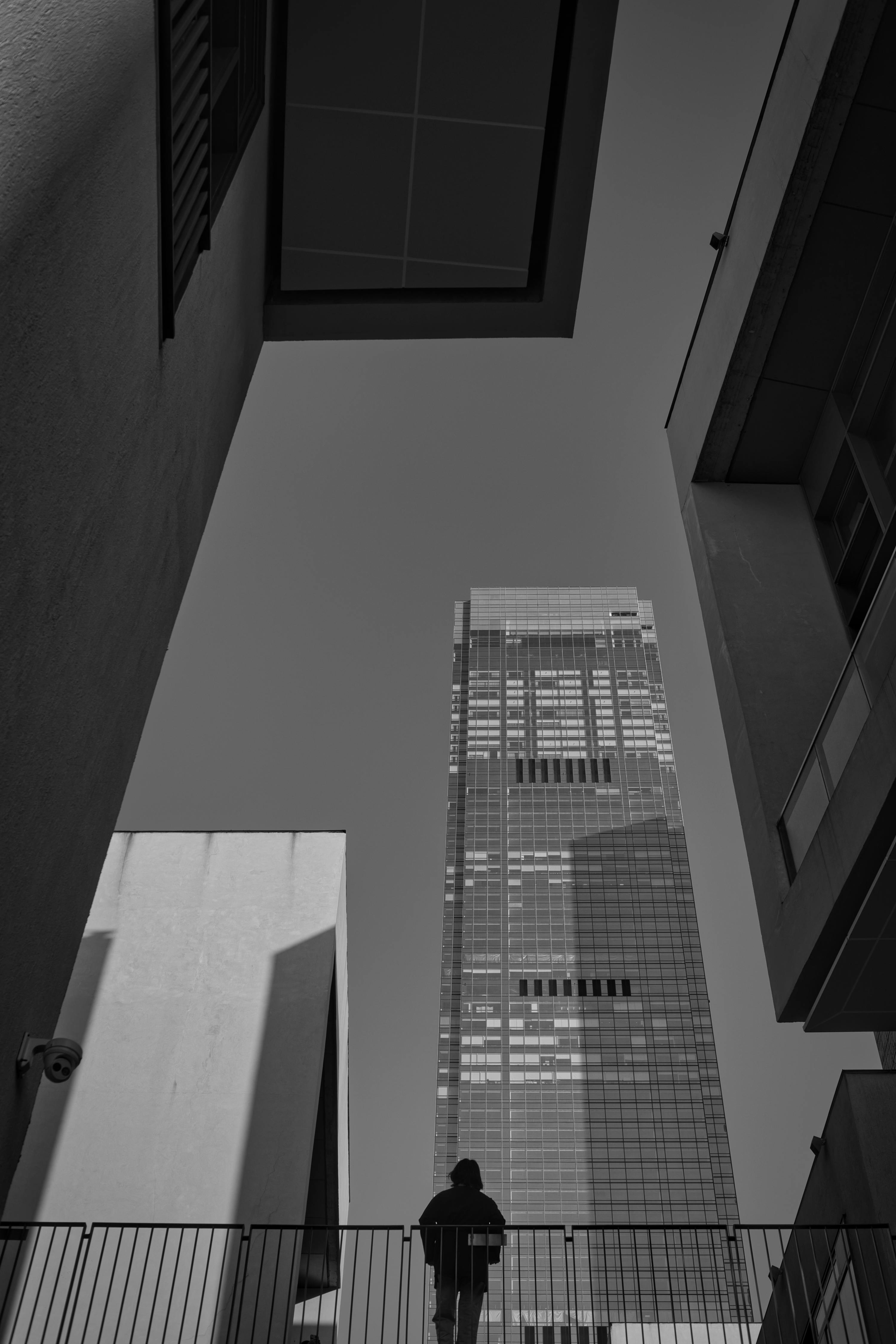 Black and white view of a skyscraper towering over a solitary person in an urban setting.