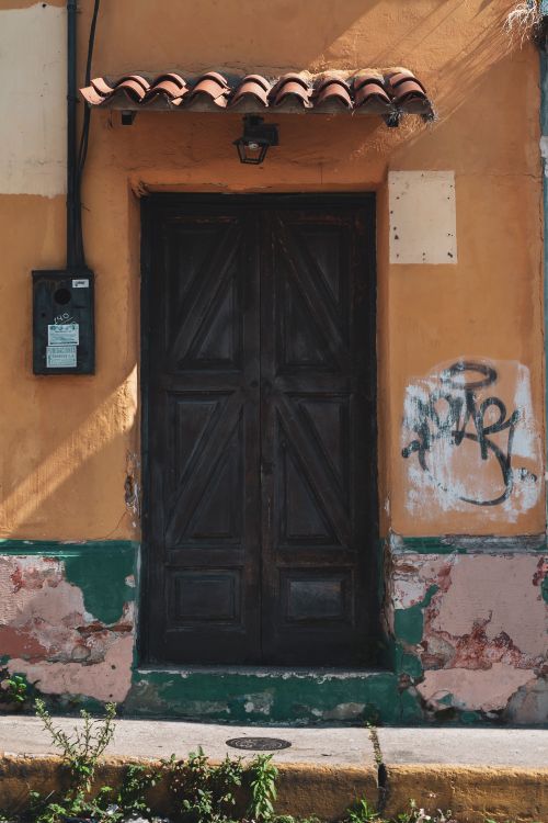 Free A vintage wooden door featuring graffiti on a weathered facade in Mérida, Venezuela, capturing rustic charm. Stock Photo
