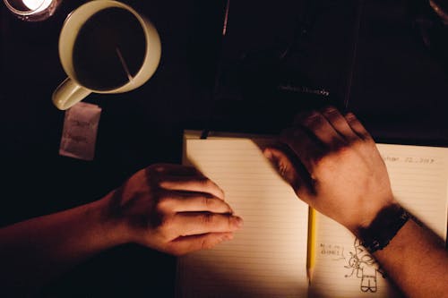 Person Holding Notebook Beside Ceramic Cup