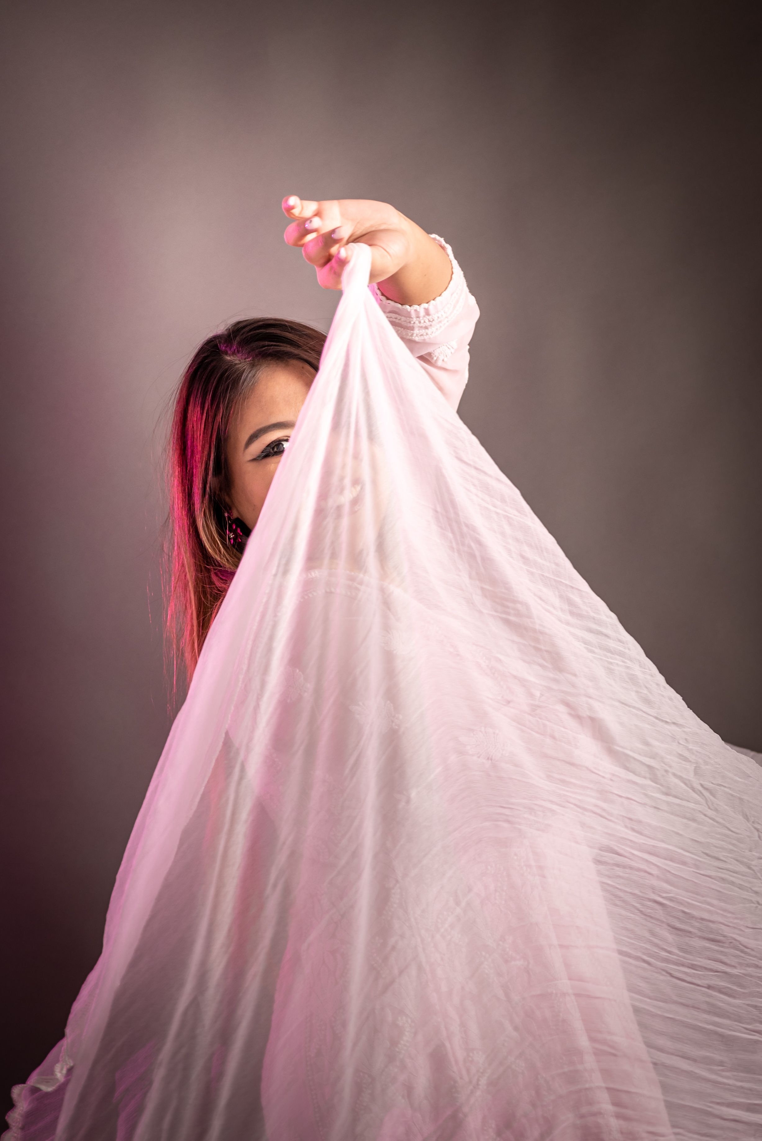 Captivating studio portrait of a woman playfully posing with a sheer pink veil. Perfect for fashion or lifestyle themes.