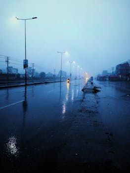 Rain-soaked street at twilight with glowing streetlights and misty atmosphere.