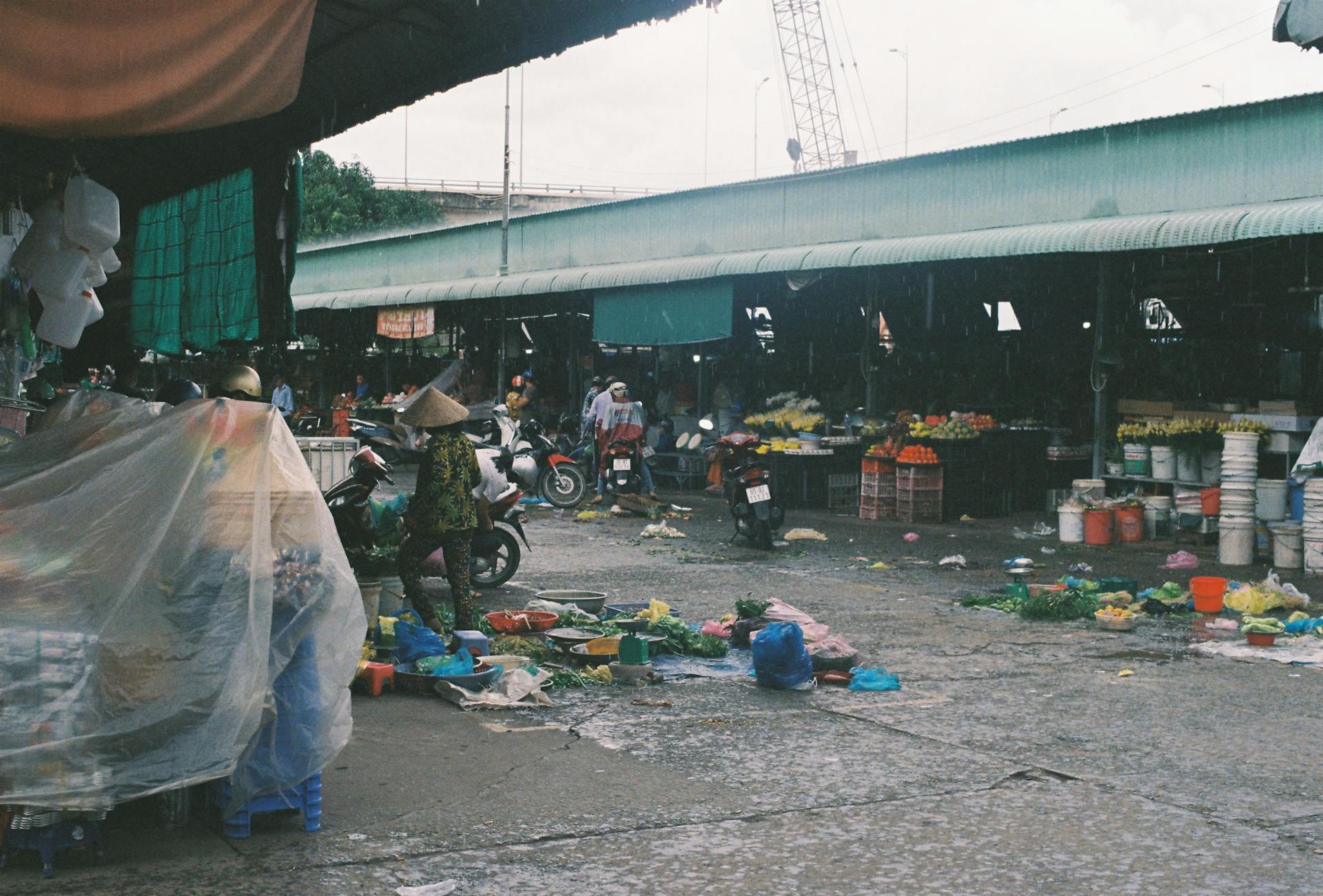 Vibrant and messy Asian market with people, goods, and motorbikes in a busy outdoor setting.