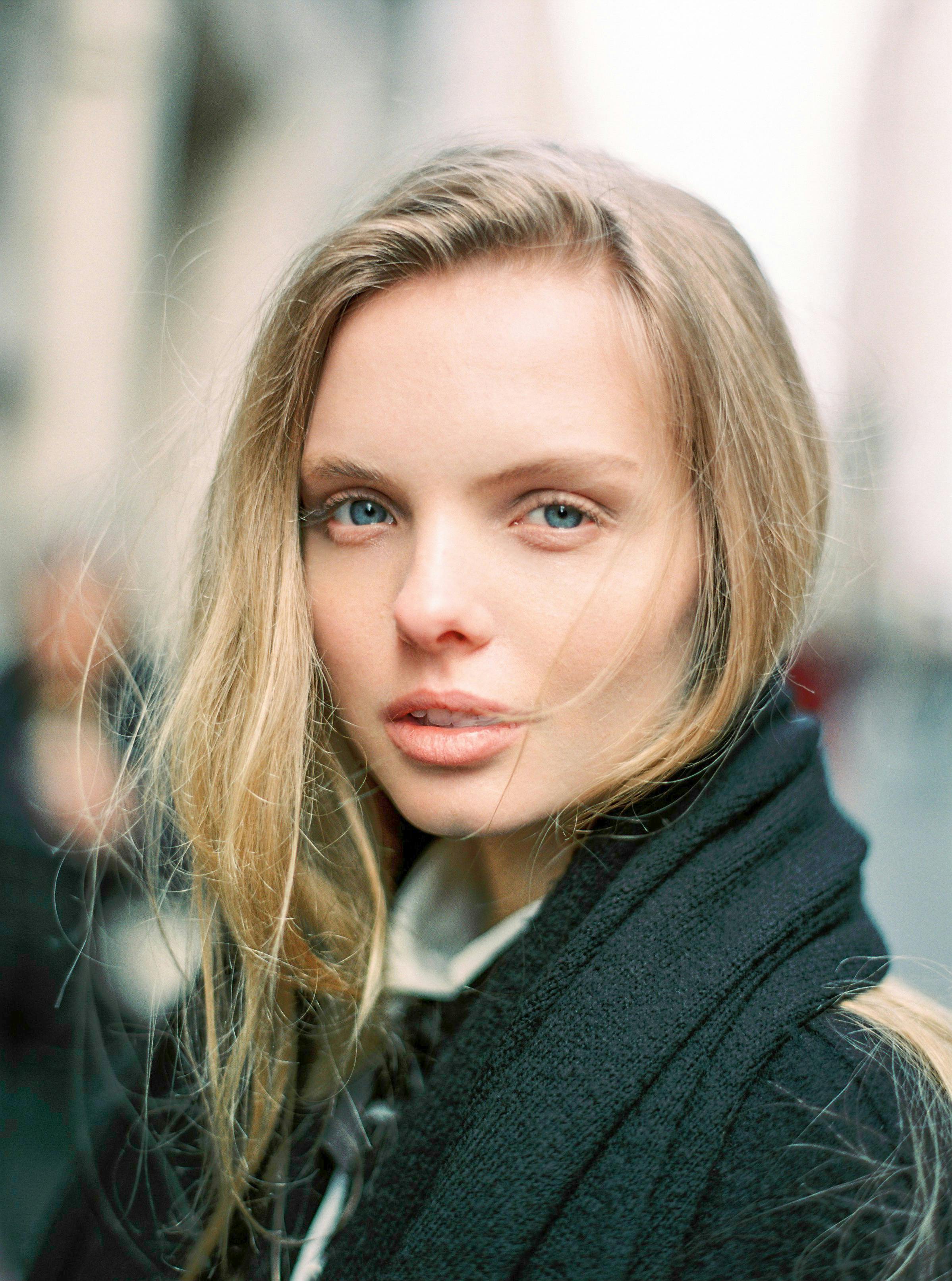 Charming close-up portrait of a blonde woman with blue eyes and a black scarf outdoors.