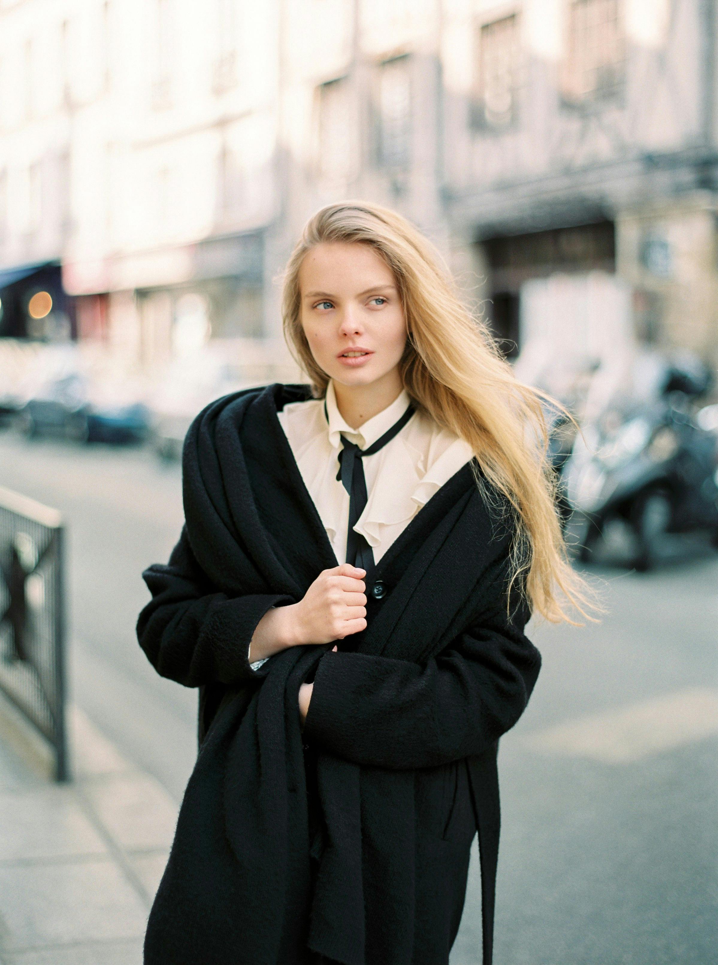 Fashionable woman in black coat and white shirt walking down a city street.