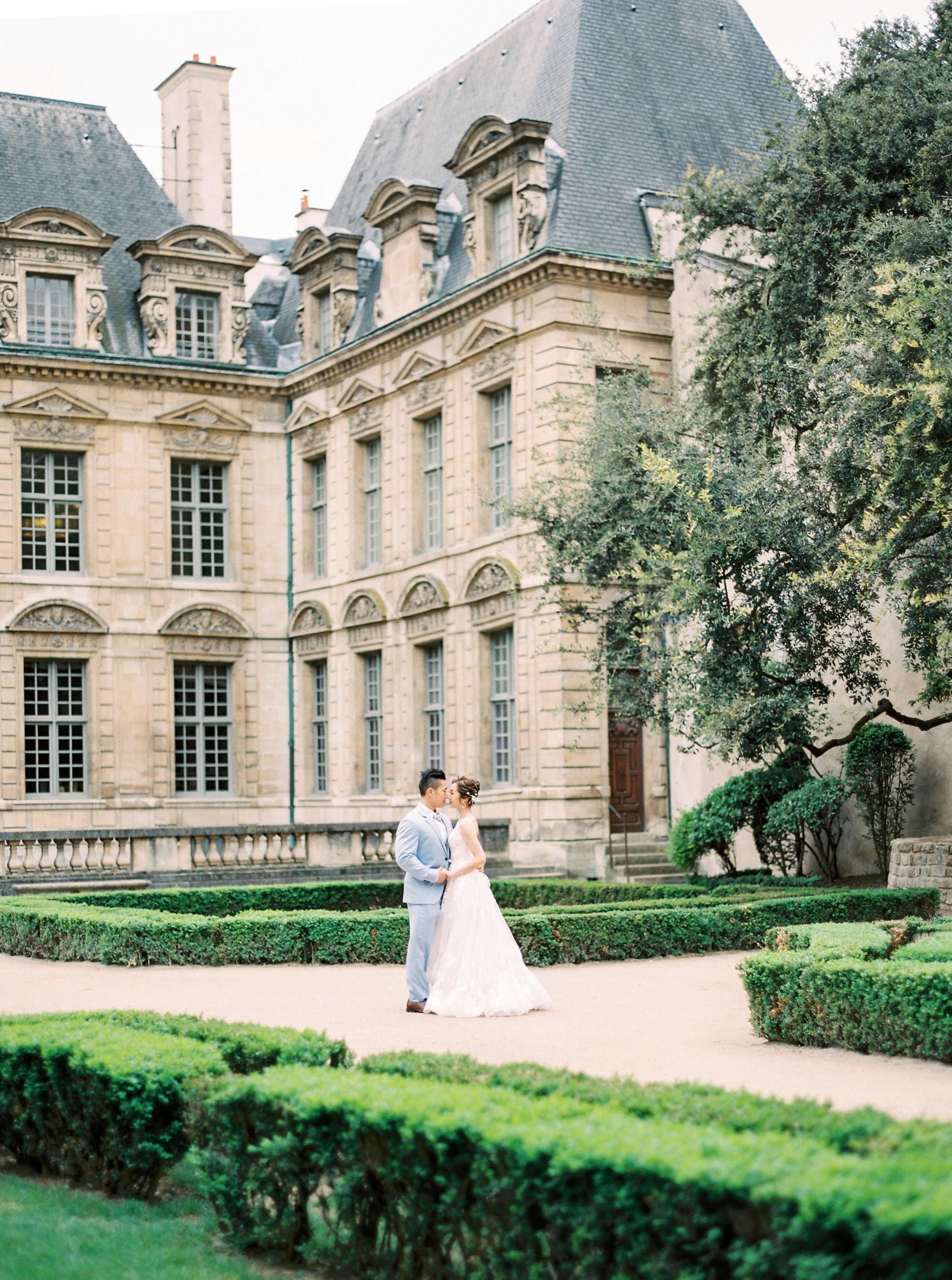 A romantic couple poses outside a historic French castle, nestled in lush gardens.