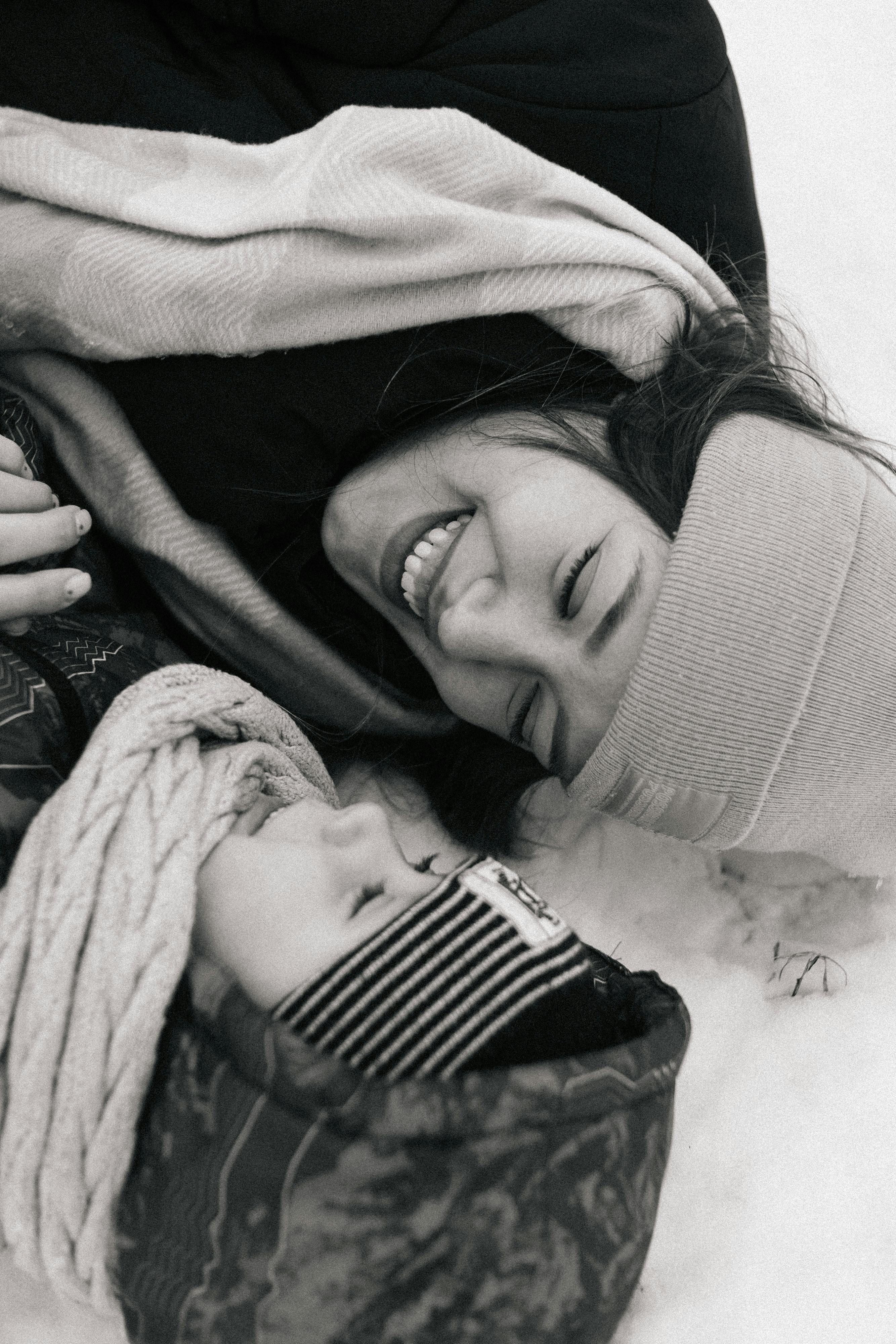 smiling woman and child lying on snow ground