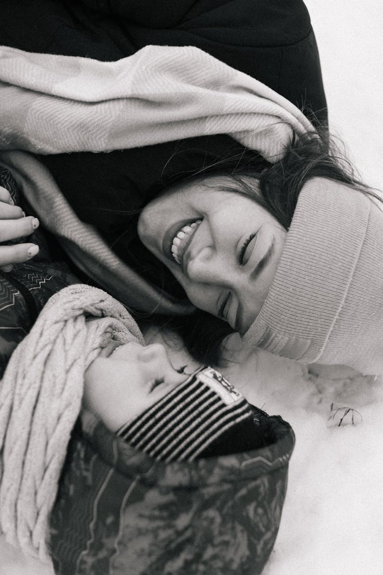 Smiling Woman And Child Lying On Snow Ground