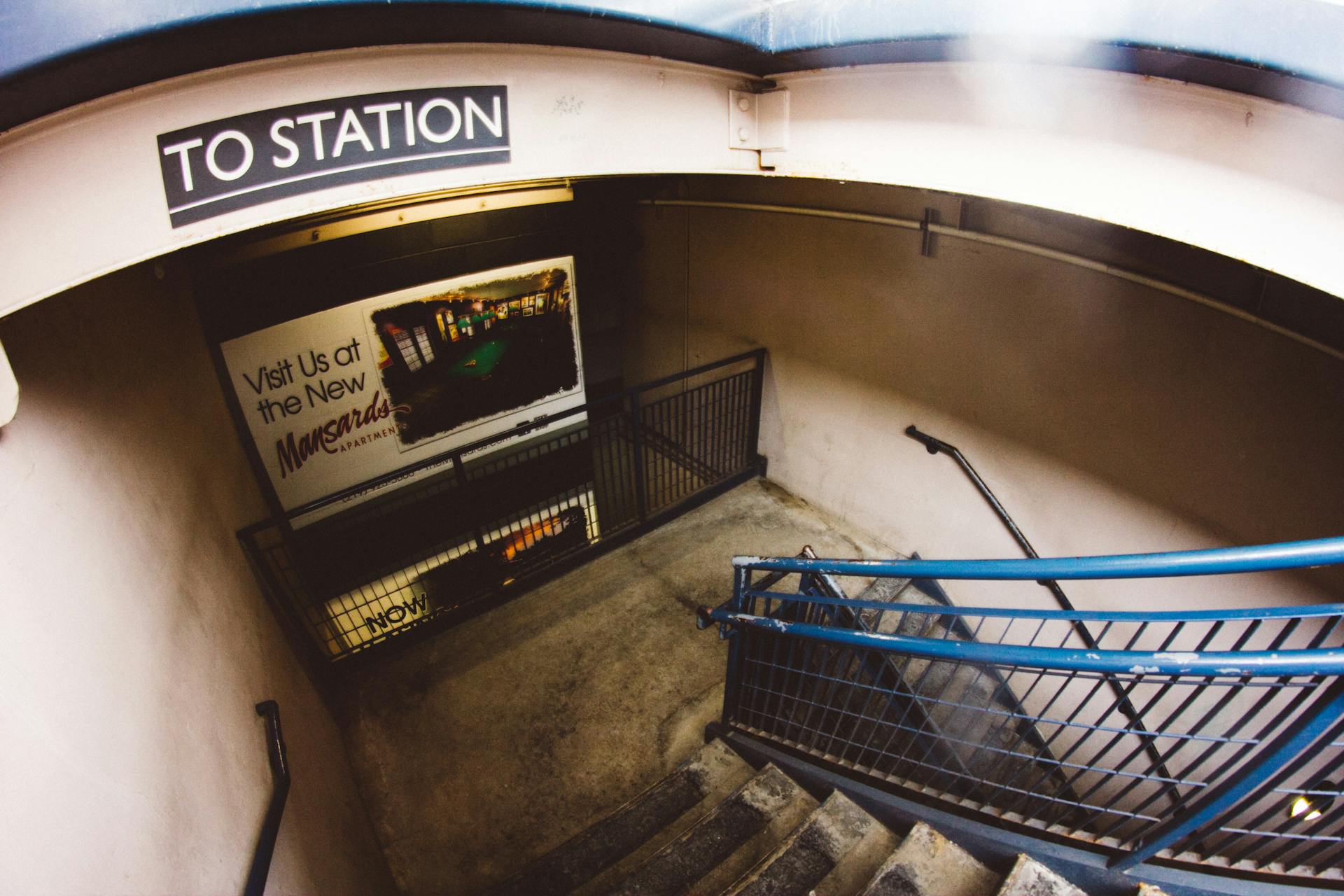 A modern urban subway station entrance featuring steel railings and promotional signage.