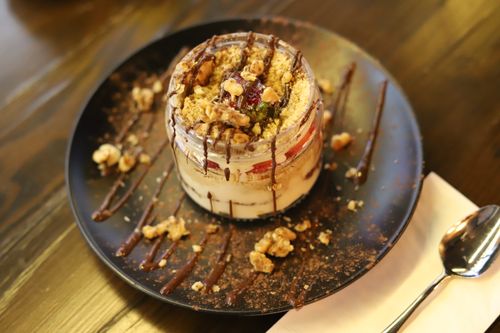 Free Tantalizing layered dessert in a jar with chocolate drizzle and nuts on a black plate. Stock Photo