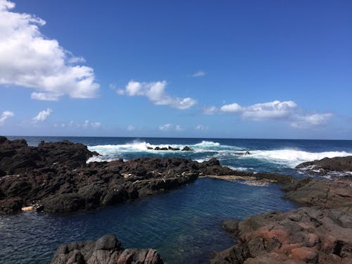 Brown Rocks Beside Ocean With Bubble Wave Under Blue Sky