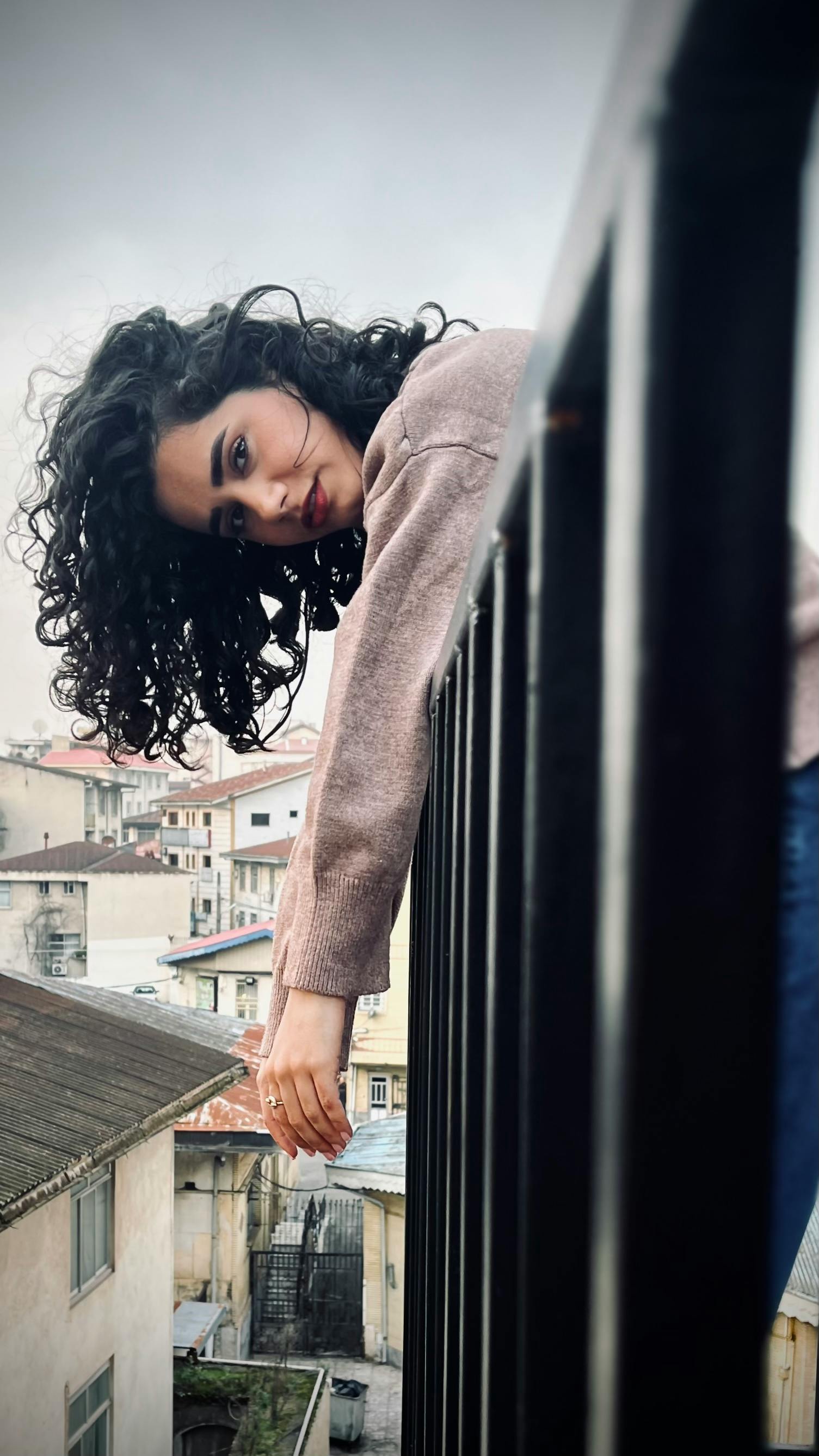 A woman with curly hair leans over a railing in urban Rasht, Iran.