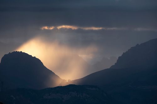 Free Sunset rays peek through clouds over Passo Pordoi, creating a breathtaking silhouette of the mountain landscape. Stock Photo