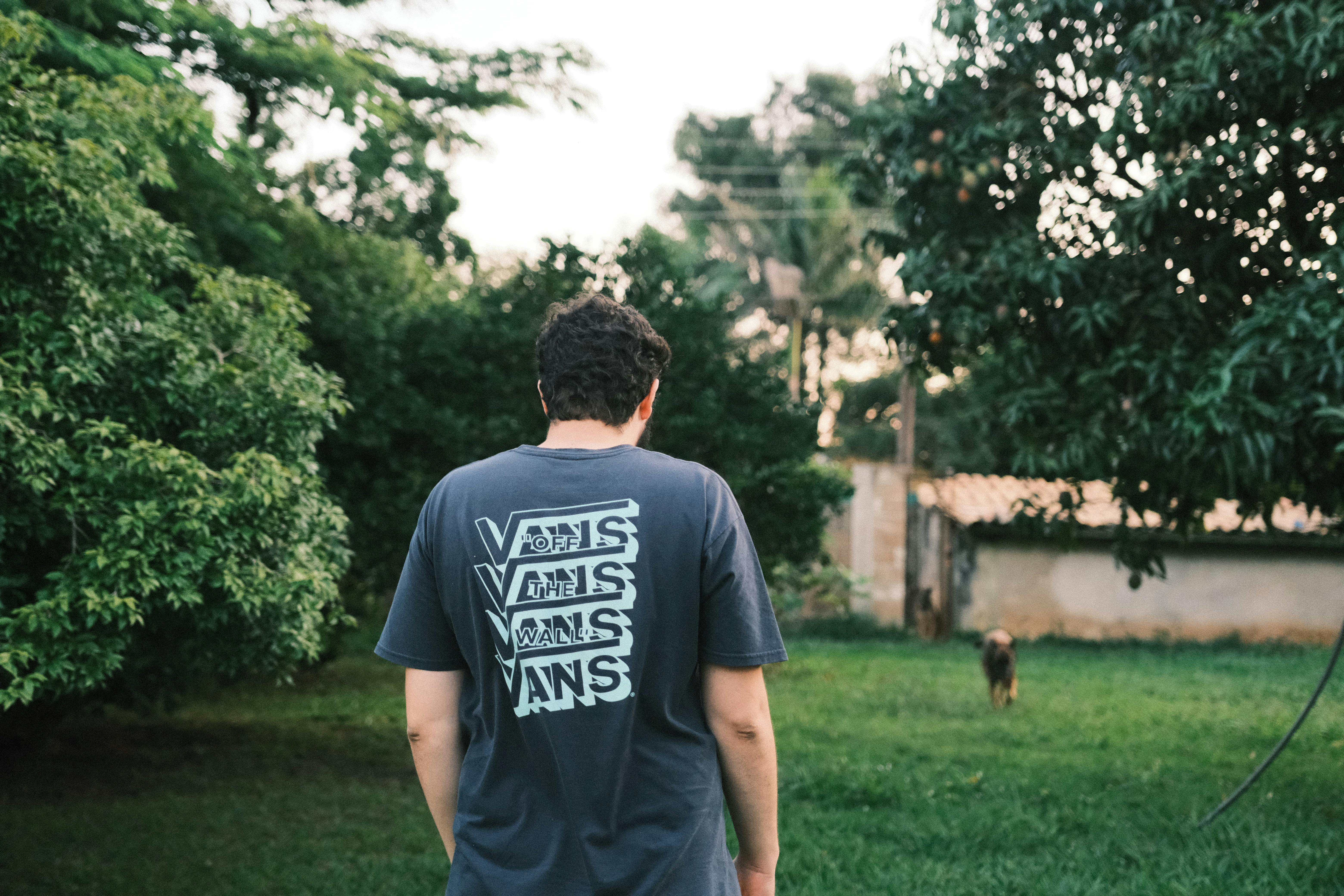 Back view of a young man in a Vans t-shirt walking through a lush garden.