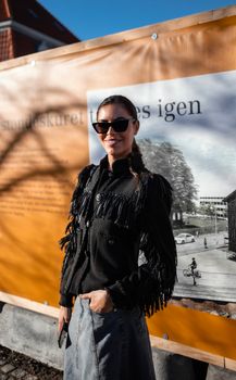 Fashionable woman smiling outdoors in sunglasses with orange backdrop.