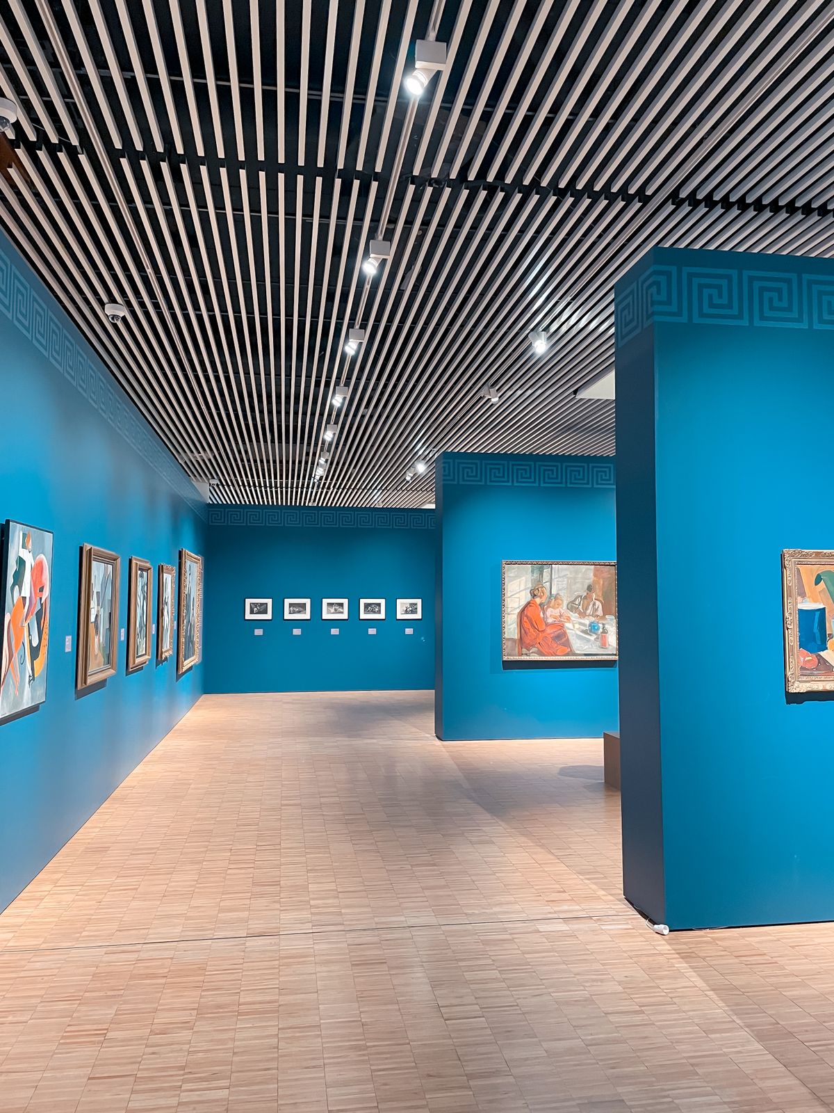 Gallery rooms with blue walls hung with framed paintings