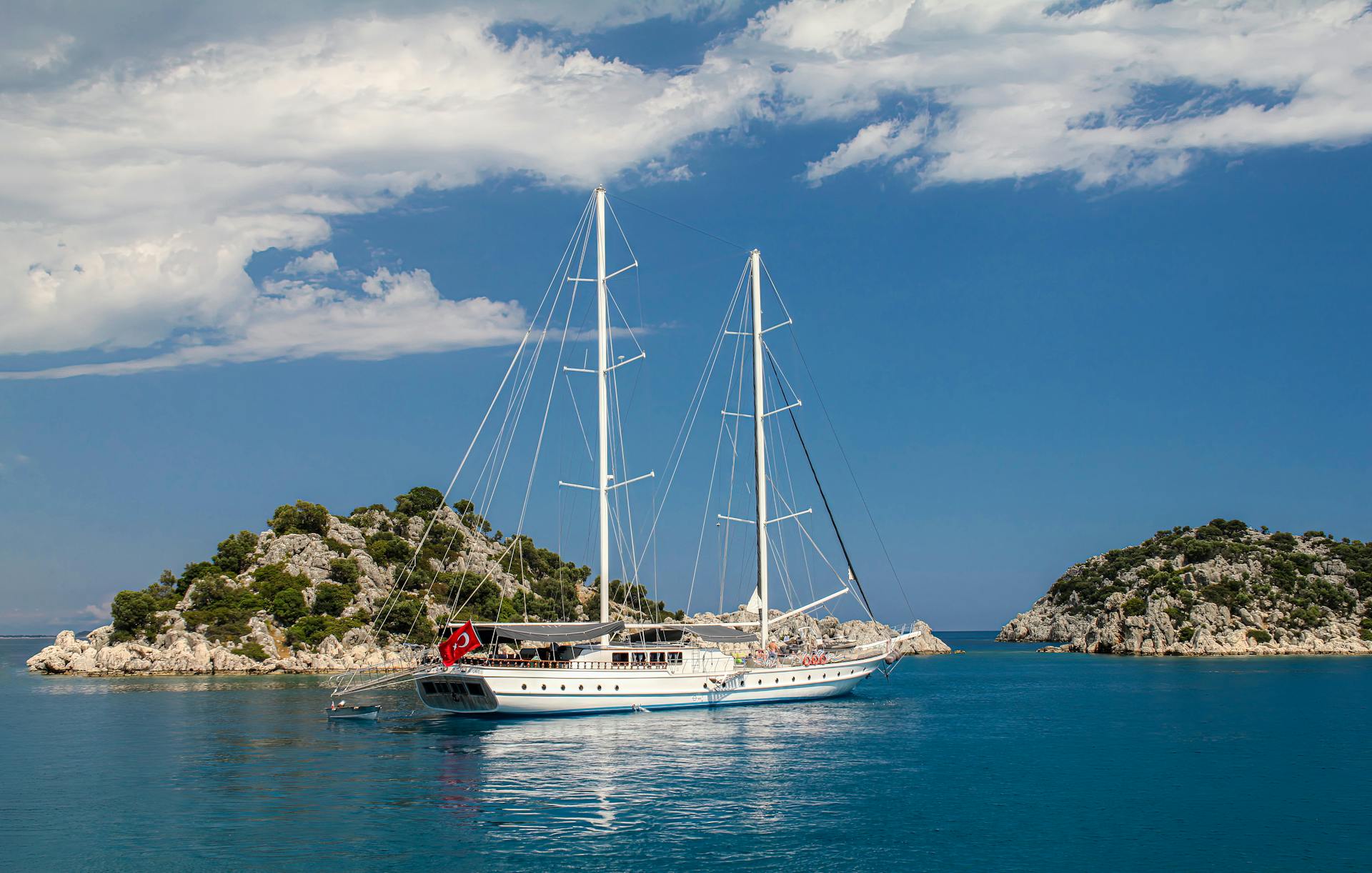 A beautiful sailing yacht anchored near rocky islands in Antalya, Türkiye, under clear blue skies.