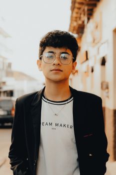 Portrait of a young man wearing eyeglasses and a blazer in a city street.
