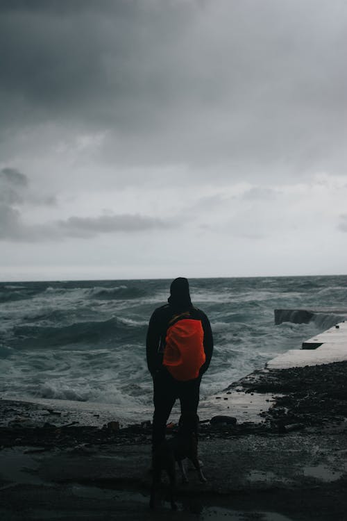 Man Standing on Sea Shore under Clouds