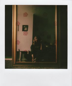 A woman reflected in a vintage mirror in a cozy room with floral decorations.