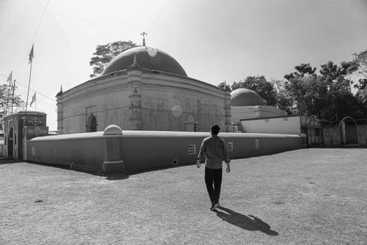 A man walks towards a historical dome structure in a sunny outdoor setting.