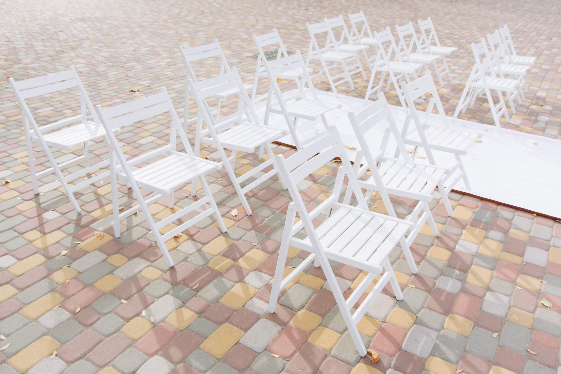 An arrangement of white folding chairs placed on colorful patterned pavers in an outdoor setting.
