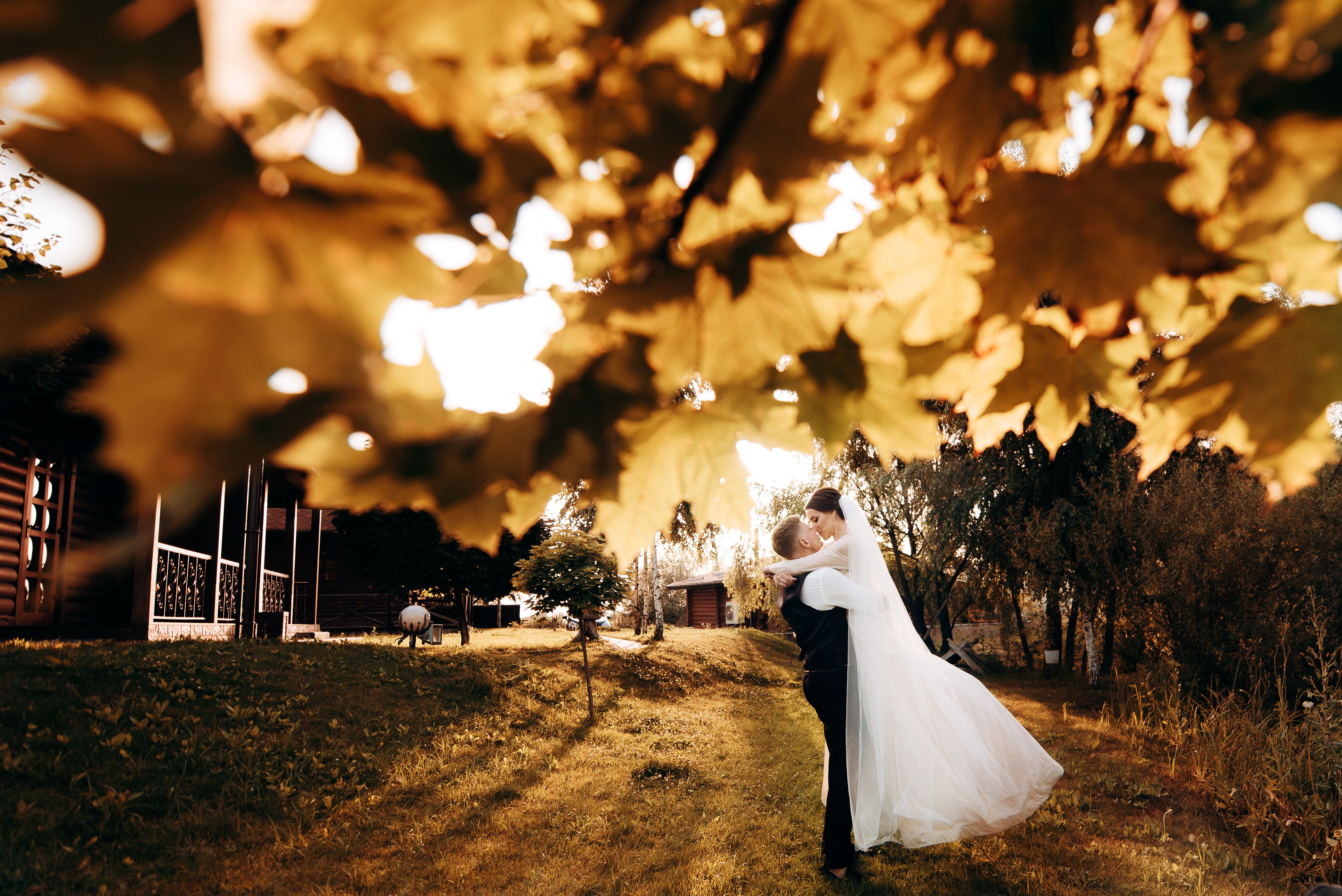 Bride and groom kissing under vibrant autumn leaves at a fall Texas wedding