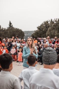 A woman addresses a large crowd during an outdoor community event, engaging with the audience.