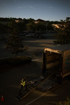 A lone worker unloading a truck during dusk in a parking area with dark surroundings.