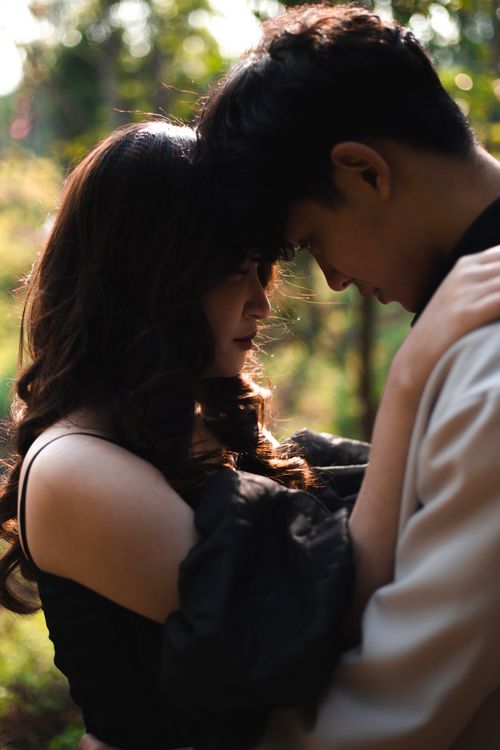 Free A romantic couple embraces in a sunlit forest creating a serene and intimate mood. Stock Photo