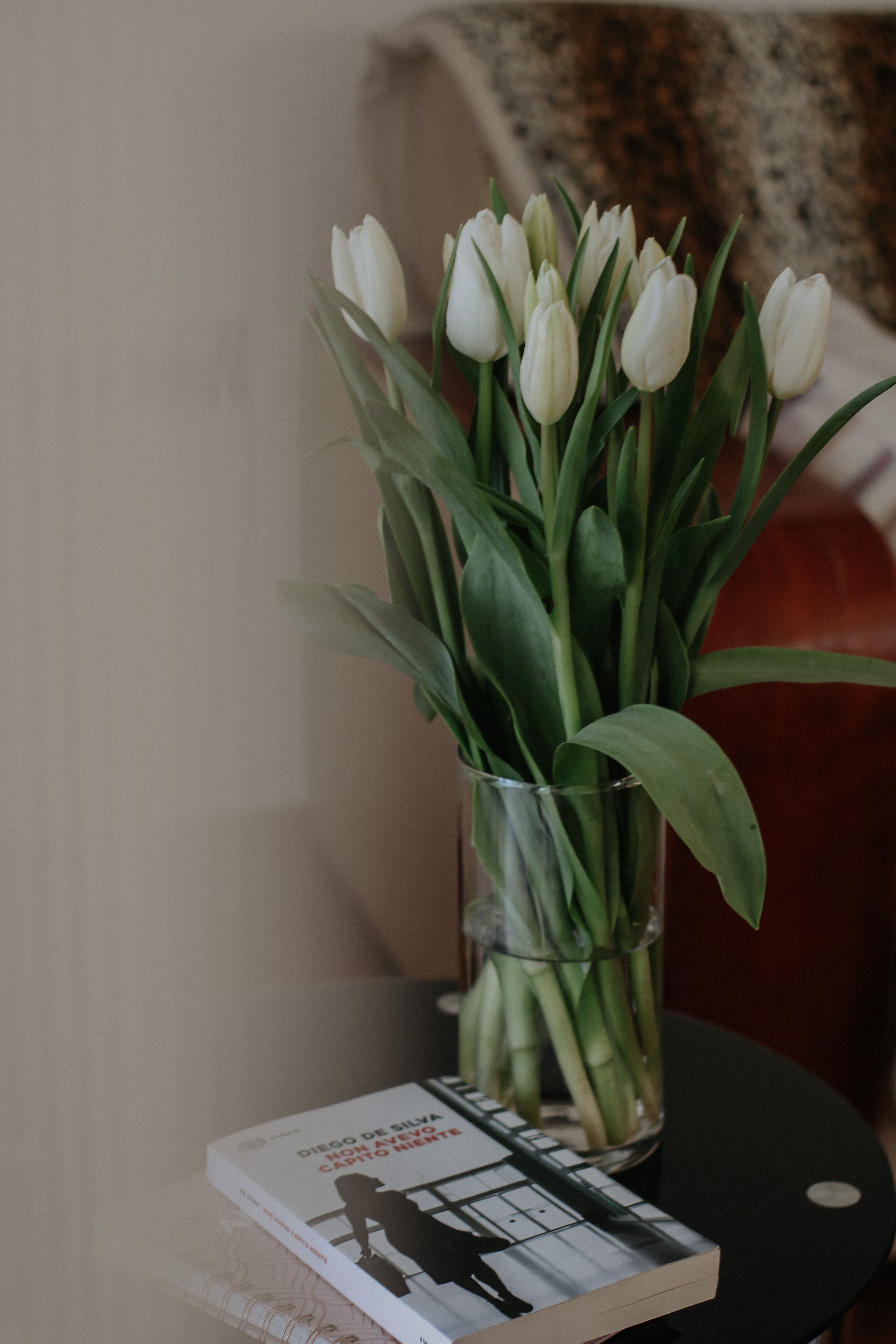 A vase of fresh white tulips placed on a table beside a book, creating a serene atmosphere.
