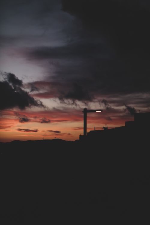 Free Silhouette of urban structures against a dramatic sunset sky with clouds. Stock Photo