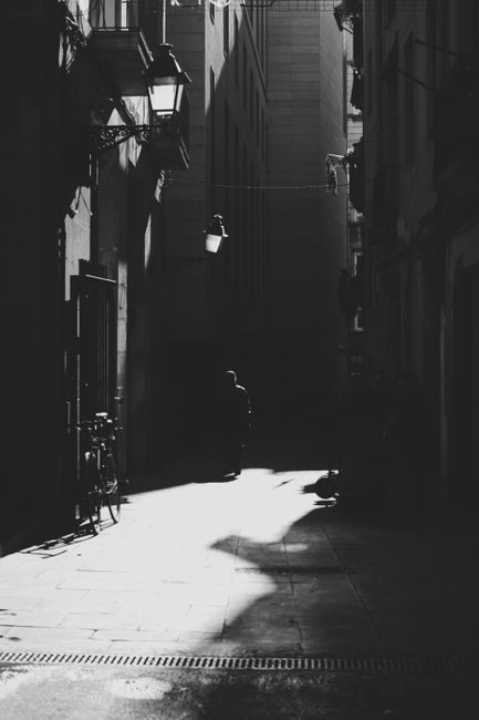 A stark black and white photograph of an empty urban alley bathed in sunlight, exuding solitude.