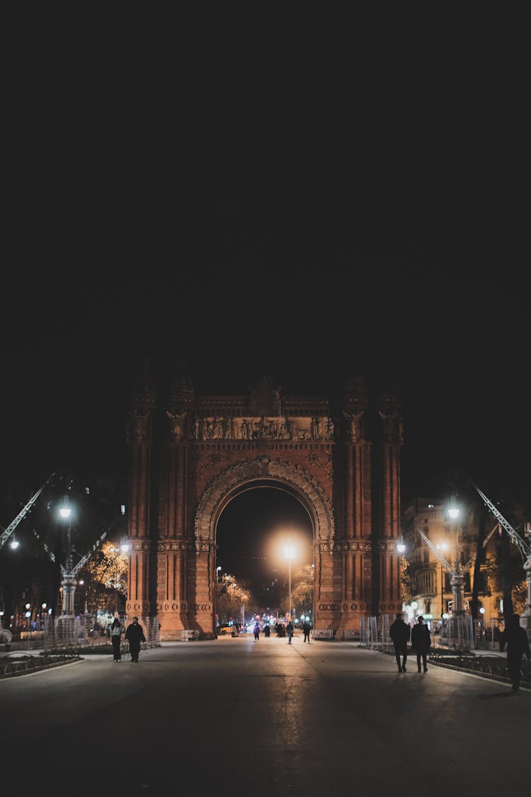 People Walking On Alley With Monument Arch At Night