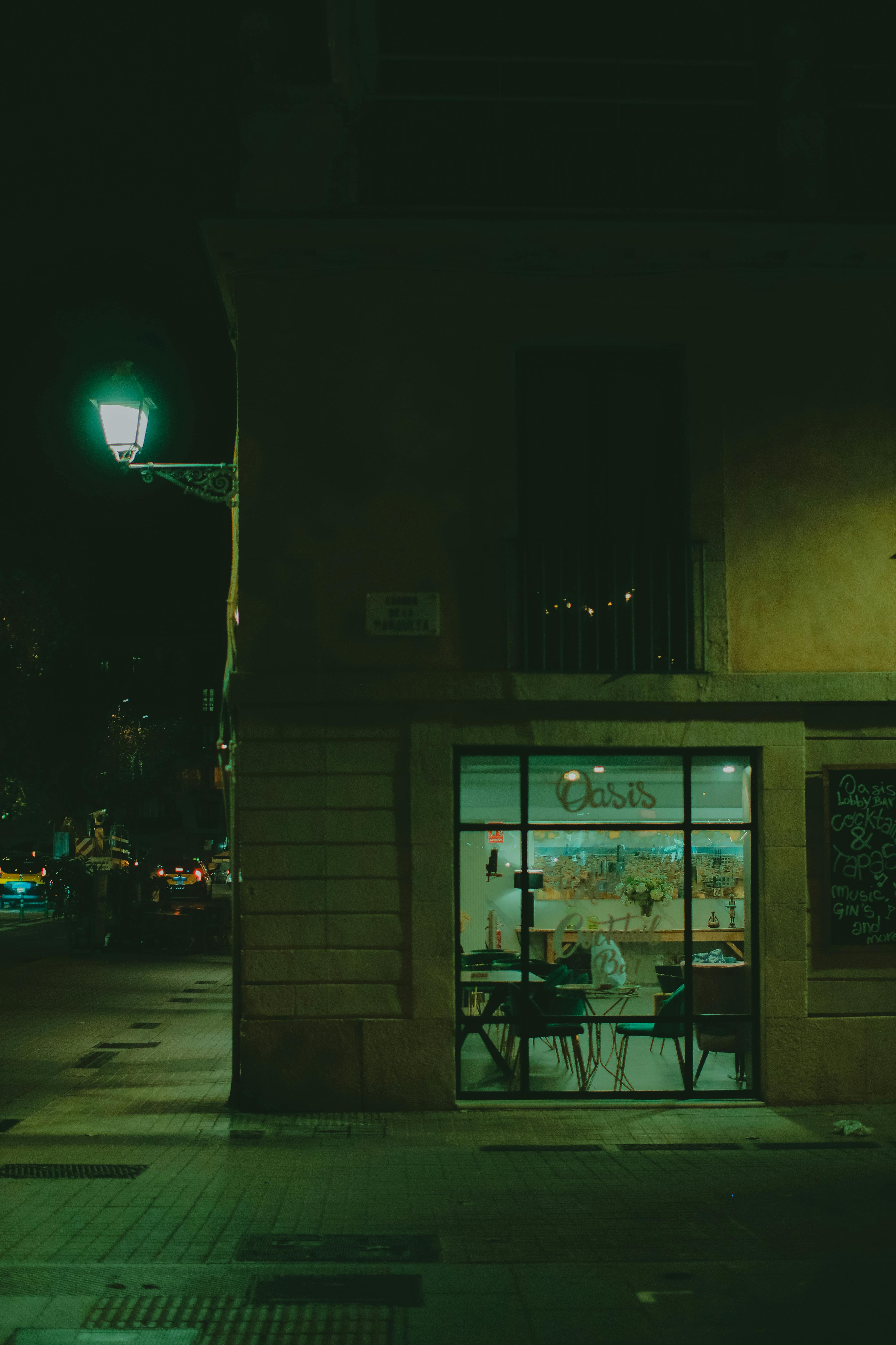 Free Nighttime view of a cozy café on a city street corner with streetlights illuminating the urban scene. Stock Photo