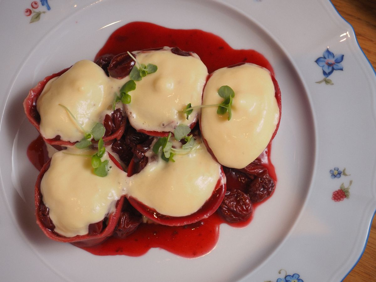 Red ravioli with sour cherries under thick cream sauce and microgreens on a plate
