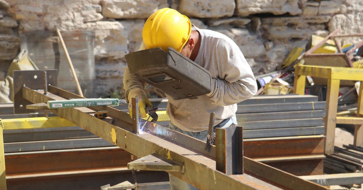 Skilled Worker Visa Sponsorship Jobs in the UK: Complete Guide — Welder wearing safety gear works with metal beams outdoors on a construction site.