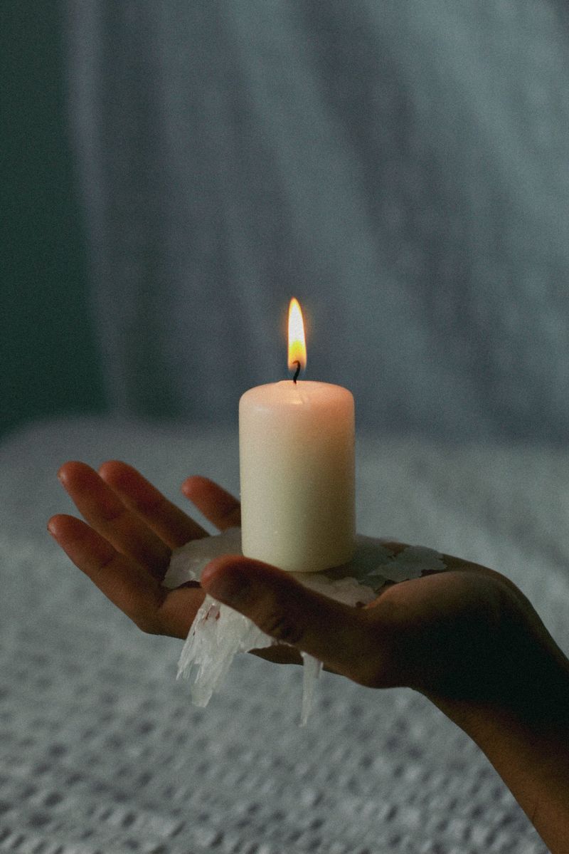 A candle resting on open palms above white cloth