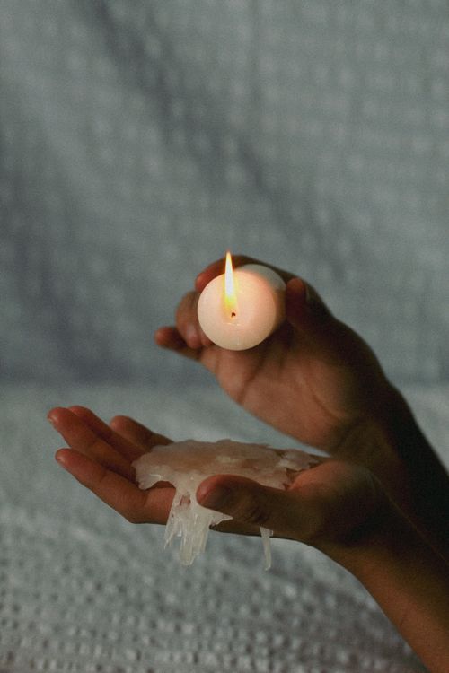 Free Close-up of hands holding a burning candle with melted wax against a textured backdrop. Stock Photo