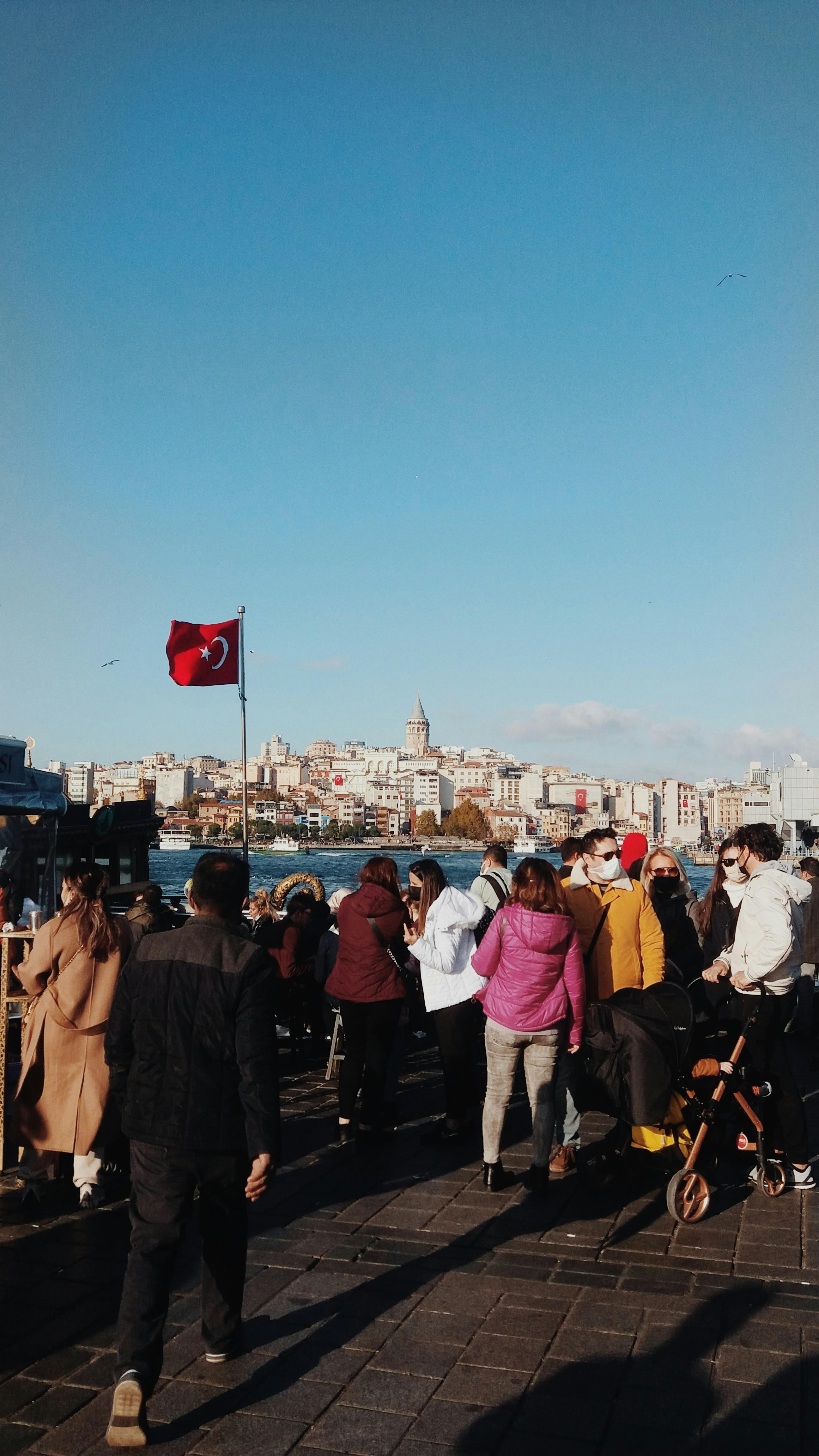 Crowd gathers by the water with Galata Tower in the background, Istanbul's vibrant cityscape.
