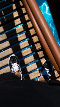 View of man's feet in sneakers standing on a wooden bridge over a sunlit pool.