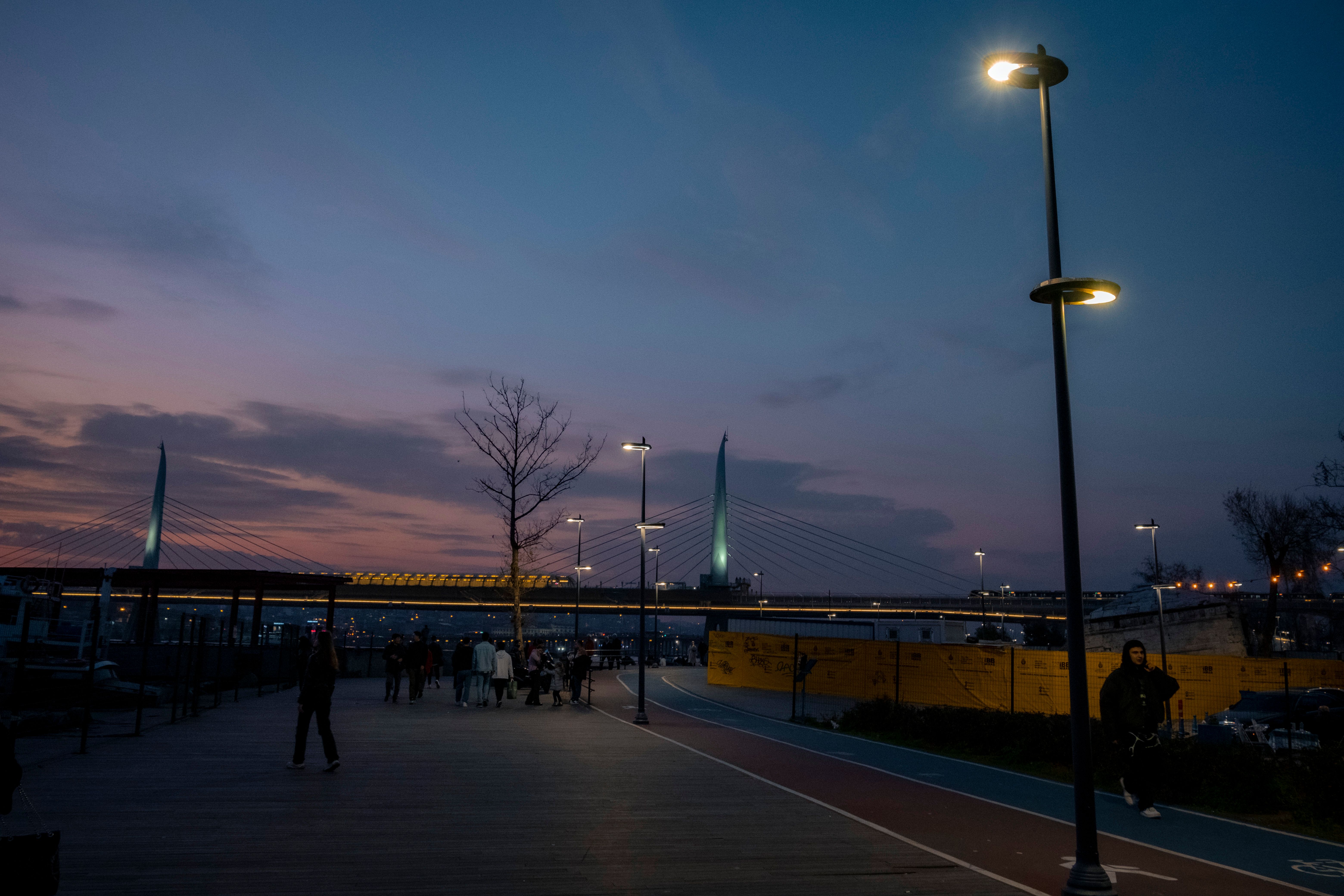 A serene evening view of a bridge promenade with people walking under street lights.